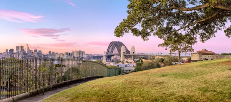 Sydney Harbour Bridge and city skyline viewed from Argyle Cut parkland at dawn.