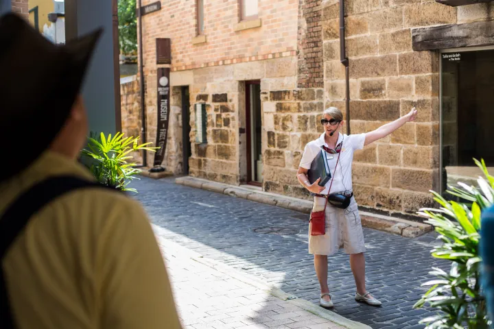 Tour guide gestures toward historic sandstone buildings during Rocks Walking Tours heritage walk.