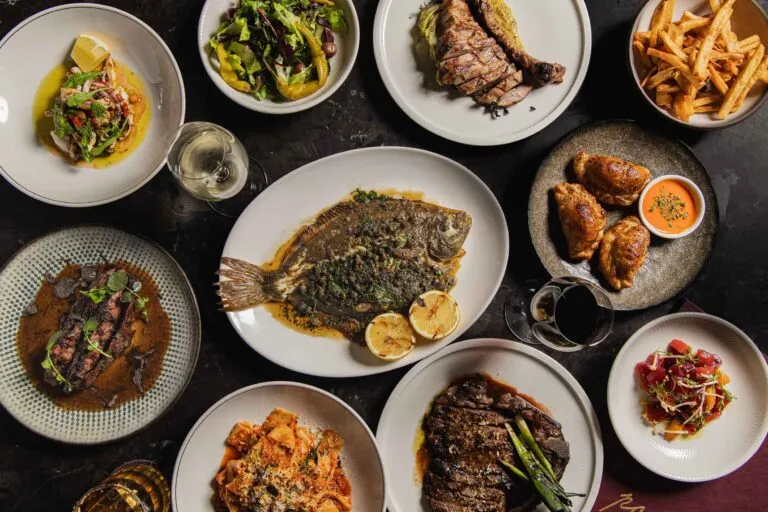 Overhead view of restaurant dishes including grilled fish, steak, fried chicken, and vegetables.