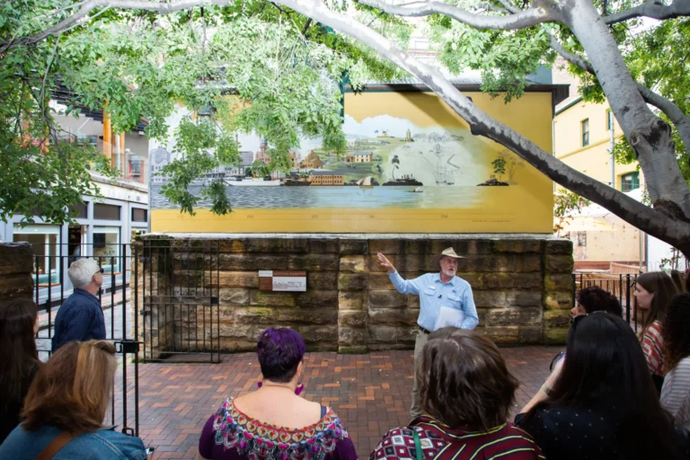 Guide presents historical Port Jackson mural to walking tour group in The Rocks.