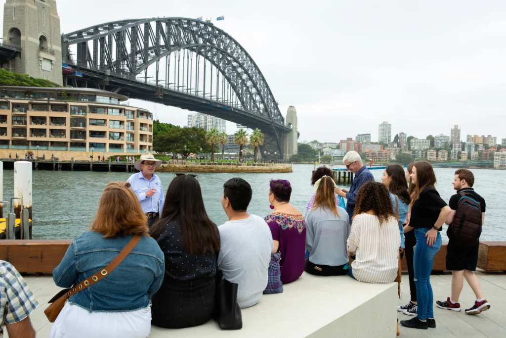 Guided tour group listening to guide on waterfront with Sydney Harbour Bridge behind.