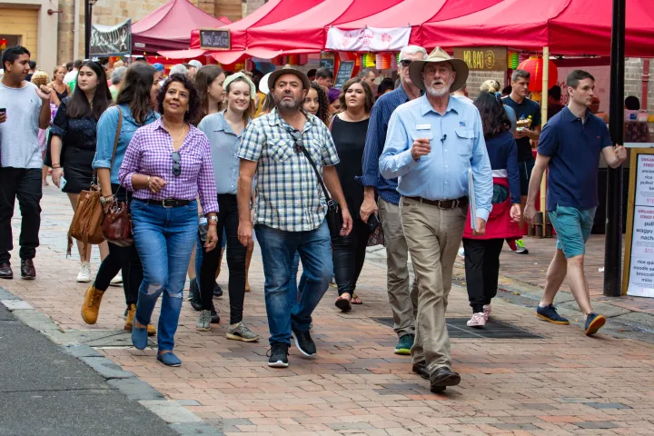 Crowds of visitors browse market stalls under pink awnings in The Rocks precinct.