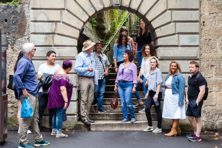 Guided walking tour group gathered at historic stone archway in The Rocks precinct.